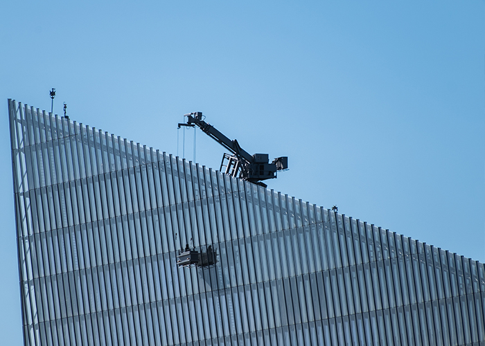 Crane operating on the rooftop of building, lifting equipment along the slanted facade.