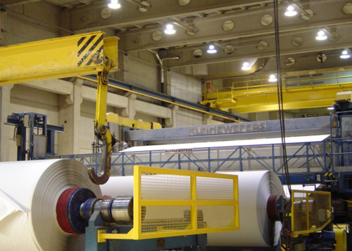 Industrial overhead crane handling large paper rolls inside a paper mill